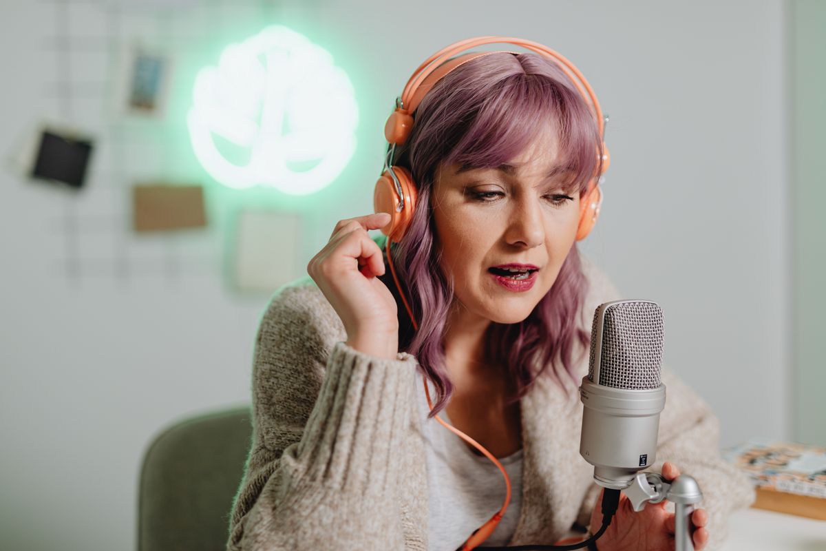 A podcast host recording at a desk, wearing headphones and speaking into a microphone